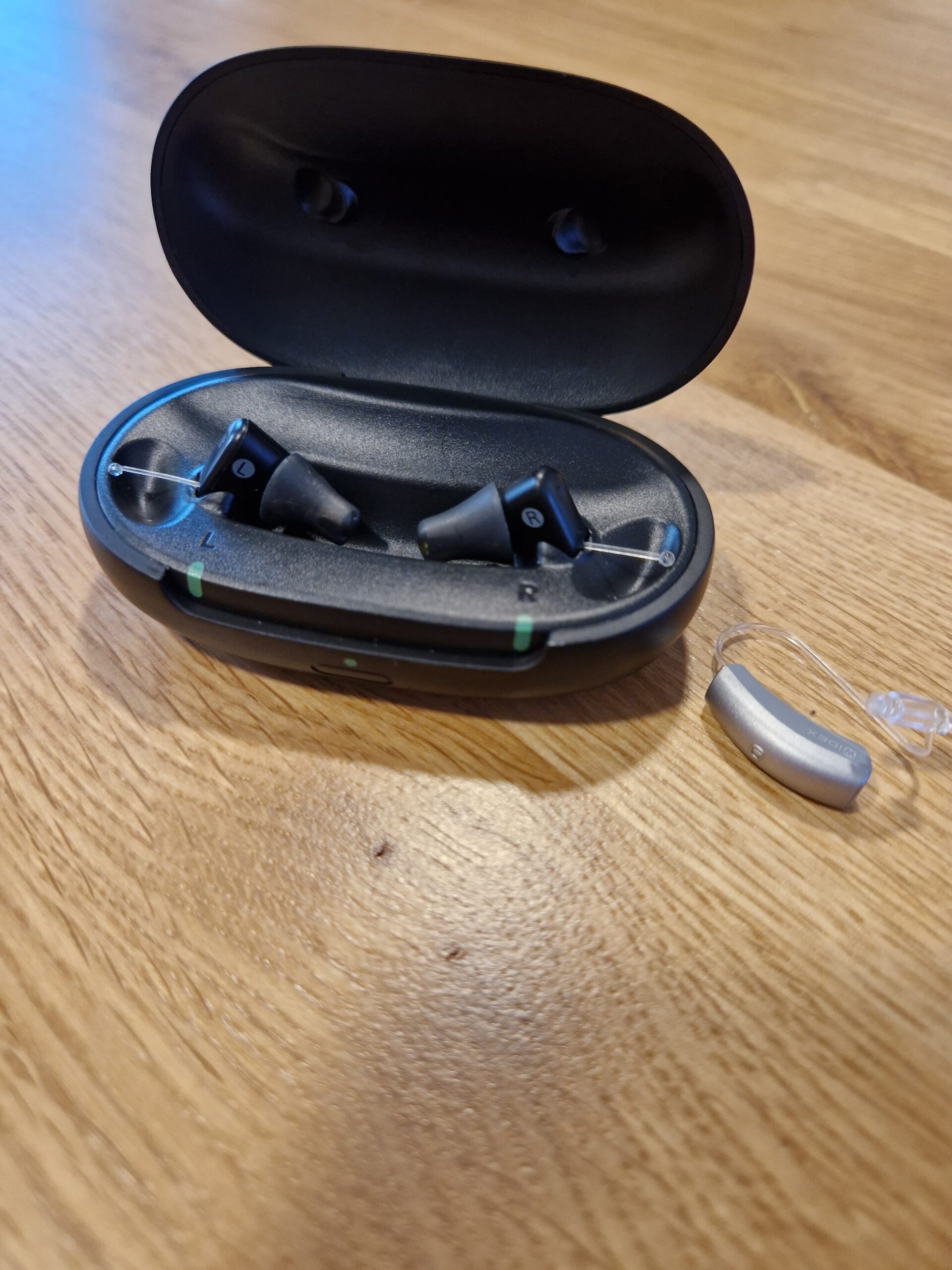 Hörgeräte Zuzahlung Unterschied. SO GEHÖRT Ladestation mit transparentem Hinter-dem-Ohr-Hörgerät. Zeigt die praktische, kabellose Aufladung und ständige Einsatzbereitschaft für den mobilen Alltag.