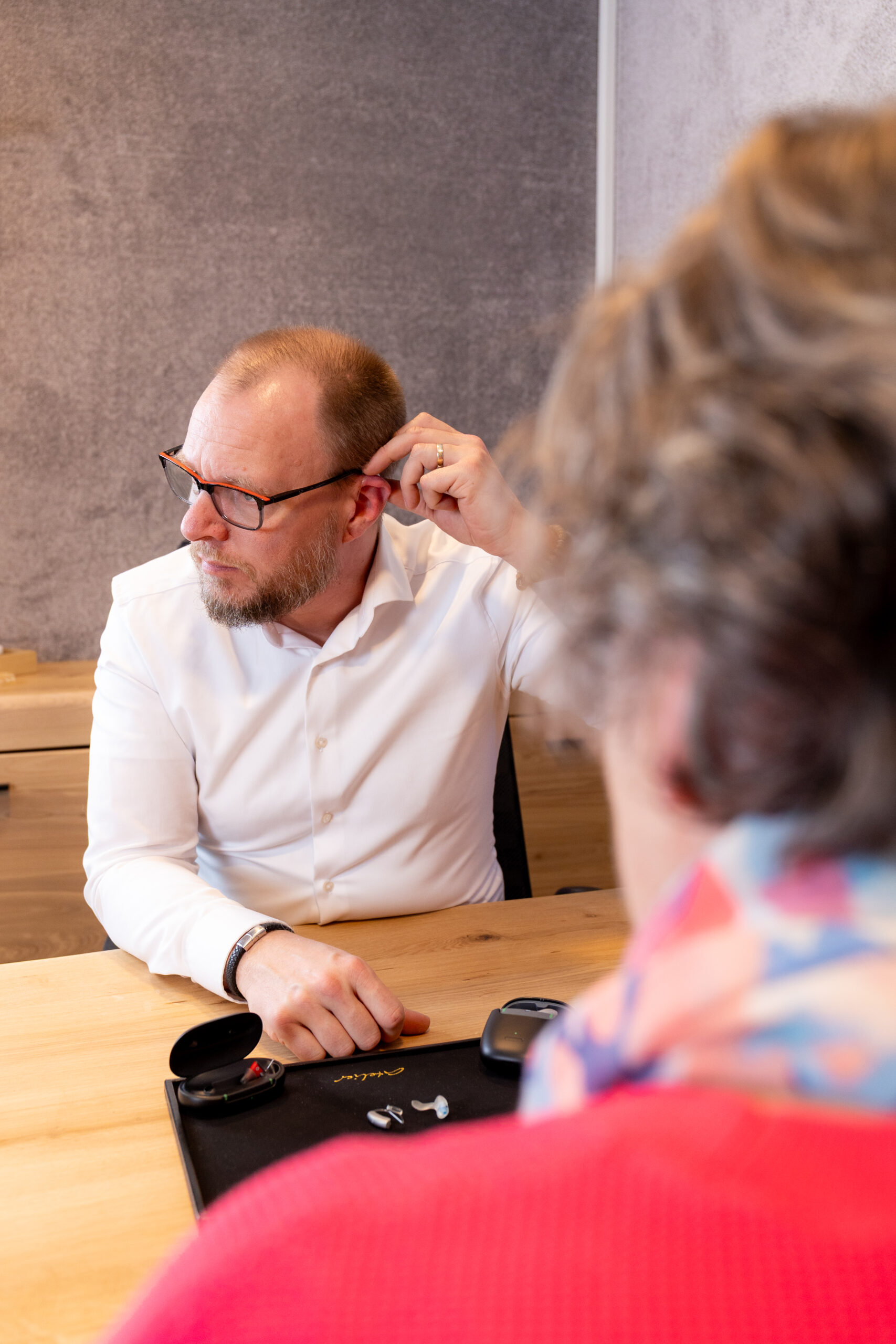 Hörberatung & Anpassung in Potsdam-Mittelmark: Sven demonstriert dem Kunden die korrekte Handhabung des Hörgeräts.